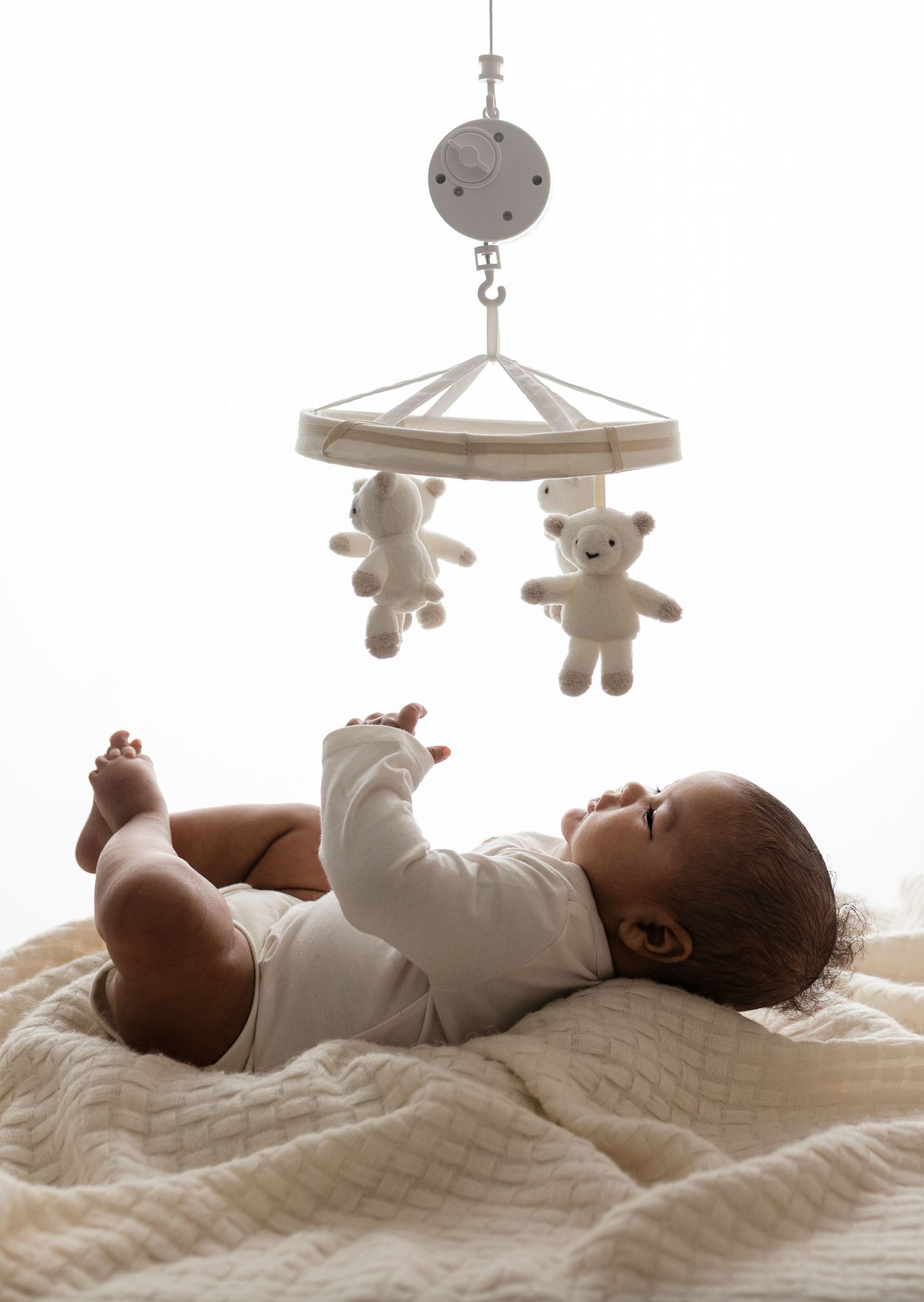 Edited backlit image by Charlottesville baby and newborn photographer shows a boy reaching toward a mobile during his milestone session.