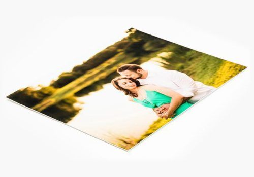 Glossy photo print of a couple embracing outdoors near a lake, displayed at an angle on a white background.