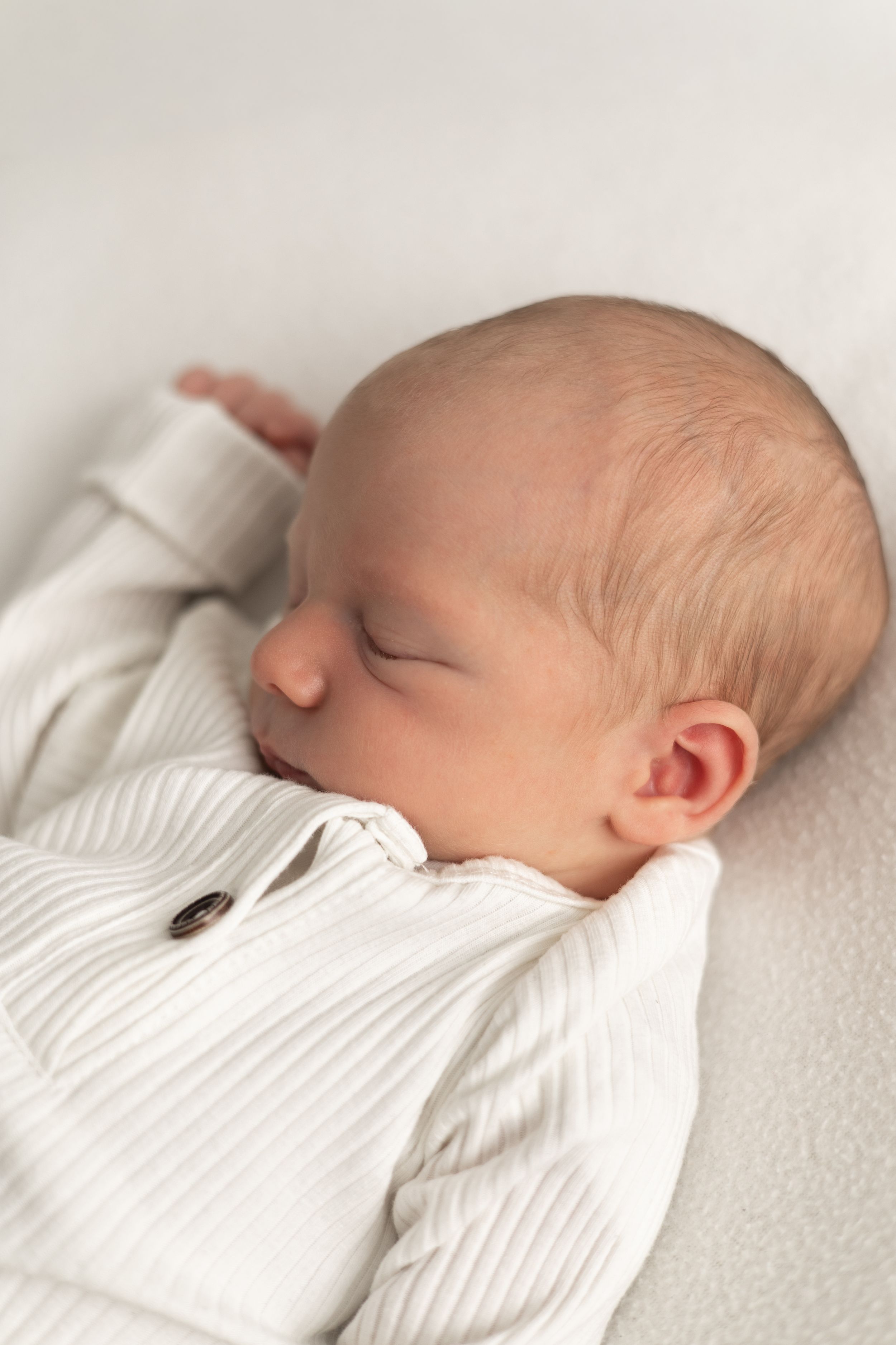 Baby photographer Nottingham peaceful newborn baby sleeping in white ribbed onesie on soft light white surface.