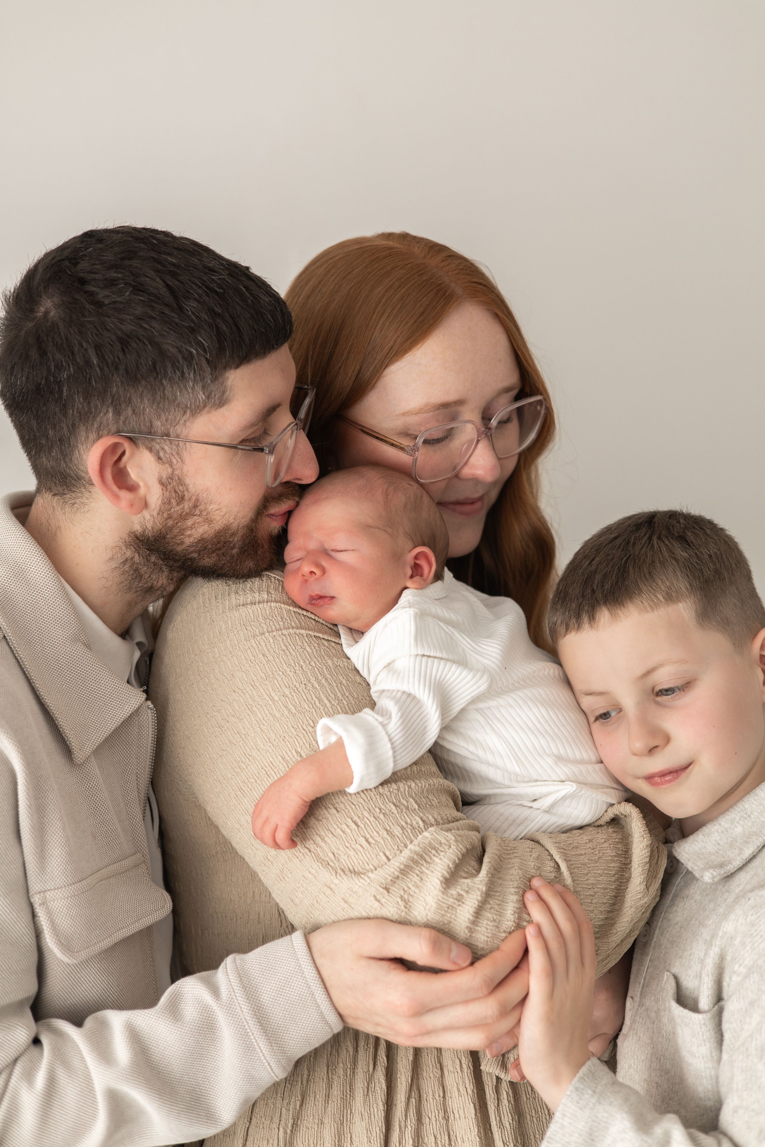 Happy family of four with parents and older son lovingly holding newborn baby together newborn photography Nottingham