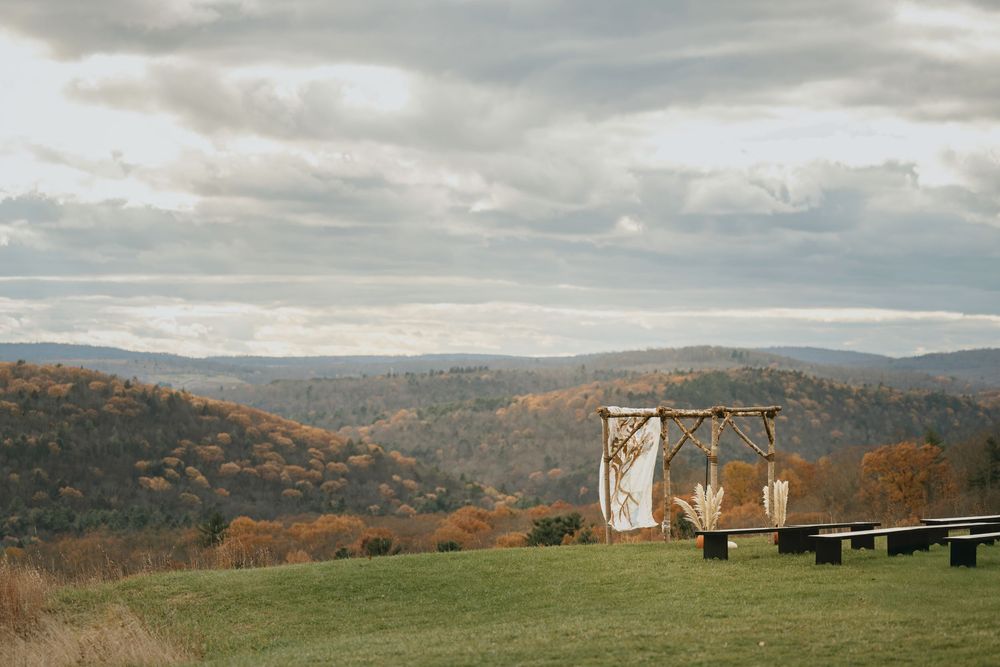 A rustic wooden arch stands on a hilltop overlooking rolling autumn mountains under dramatic cloudy skies.