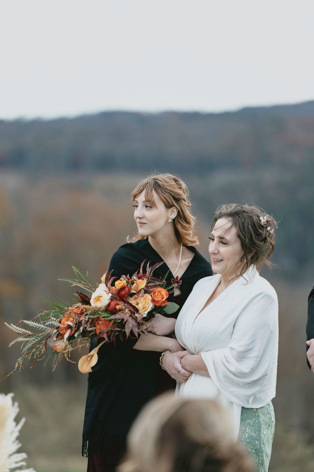 An outdoor autumn wedding ceremony with floral arrangements featuring orange blooms against a mountain backdrop.