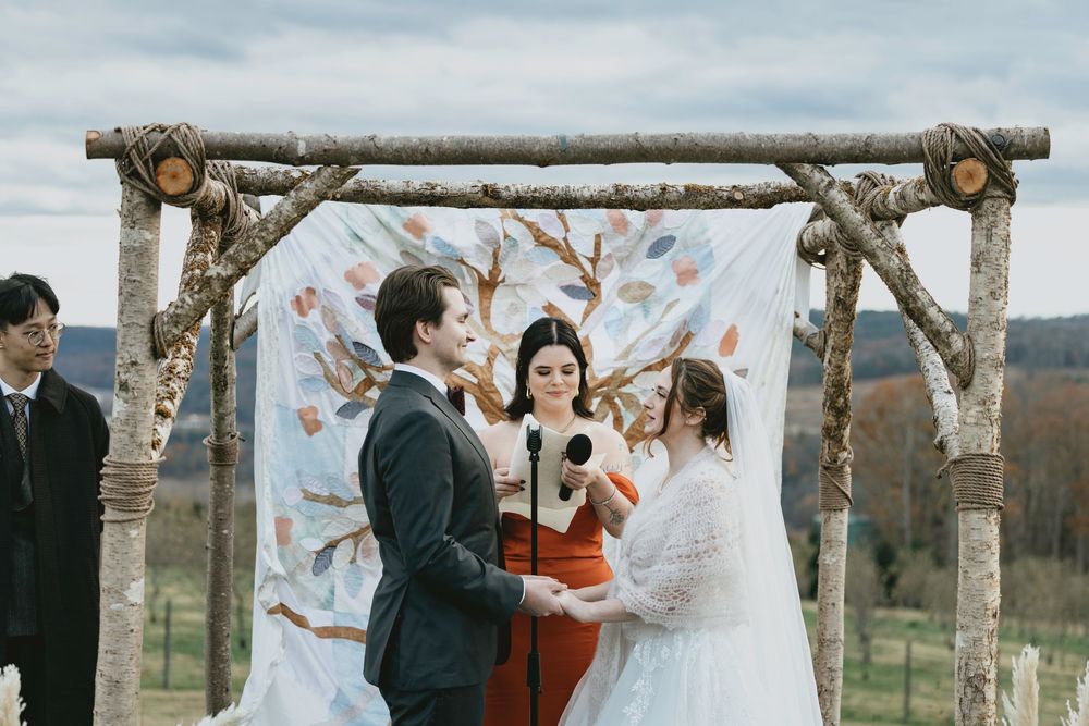 A couple shares a romantic moment during their outdoor wedding ceremony beneath rustic wooden arches and trees.