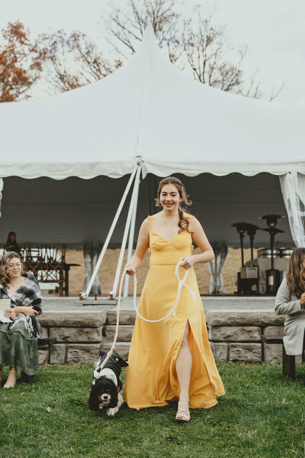 A person in a flowing yellow dress sits on stone steps under a white event tent.