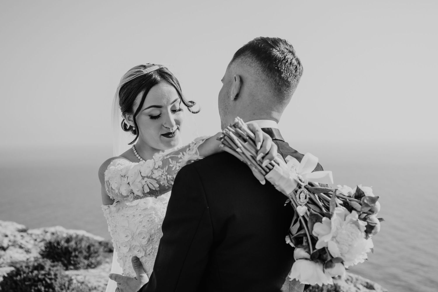 A romantic black and white wedding photo series showing tender moments between newlyweds by the ocean.