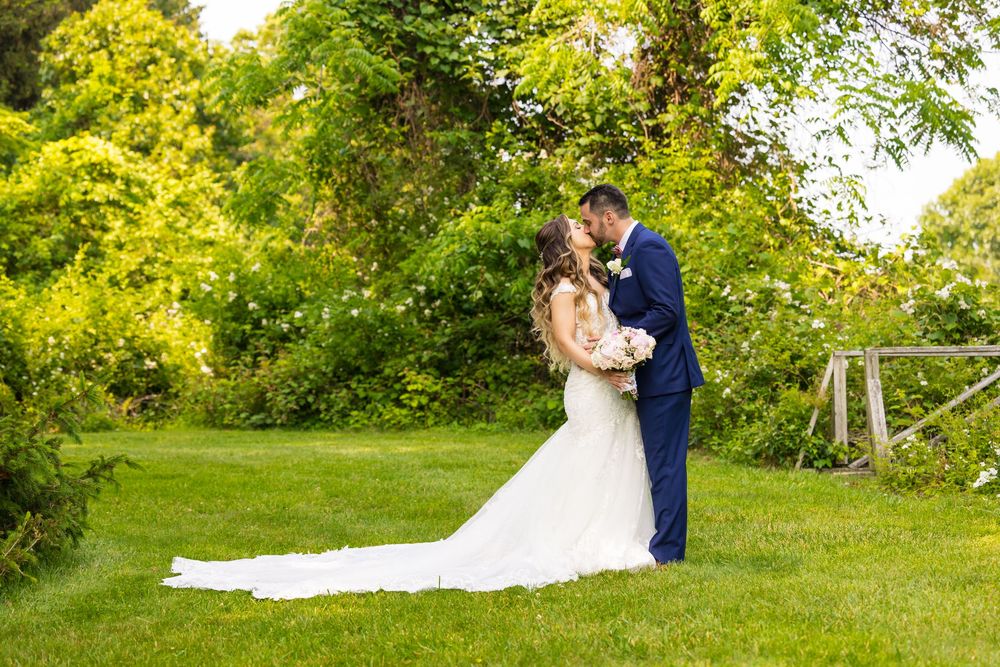 A couple in wedding attire embrace on a lush green lawn surrounded by vibrant yellow and green foliage.