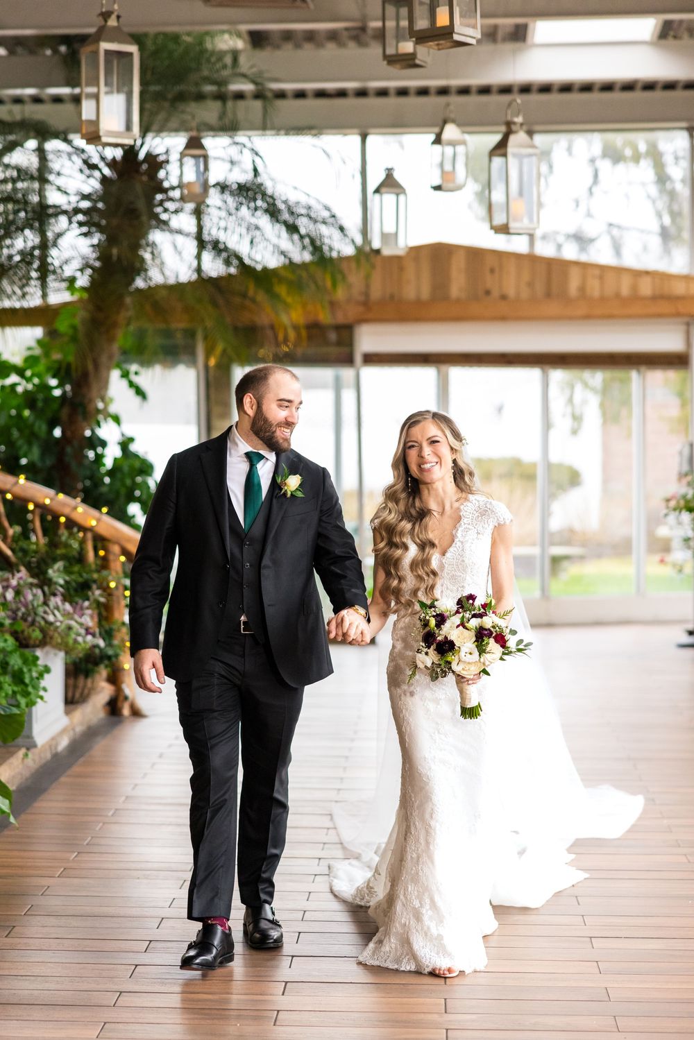 A couple walks together in a covered outdoor venue with elegant lanterns and natural lighting during their wedding day.