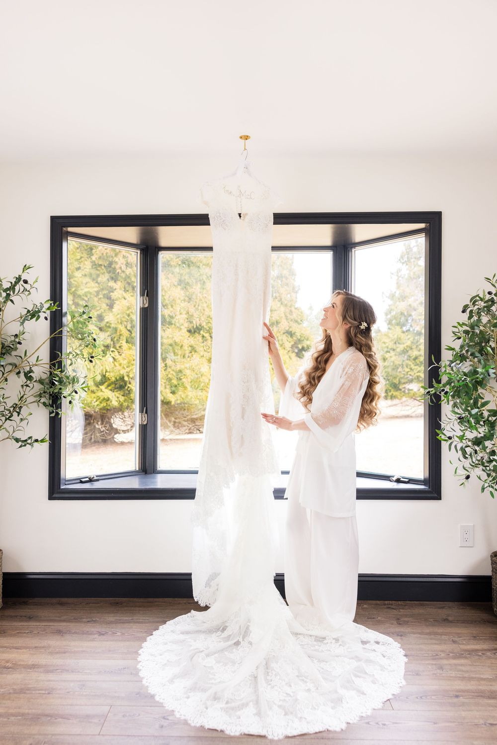 A bride in a flowing white wedding gown spins gracefully in front of large windows in a bright, minimalist room.