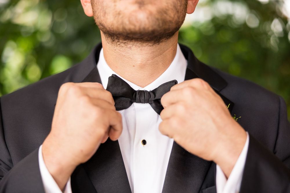 A collection of black bow ties being adjusted on formal white dress shirts.