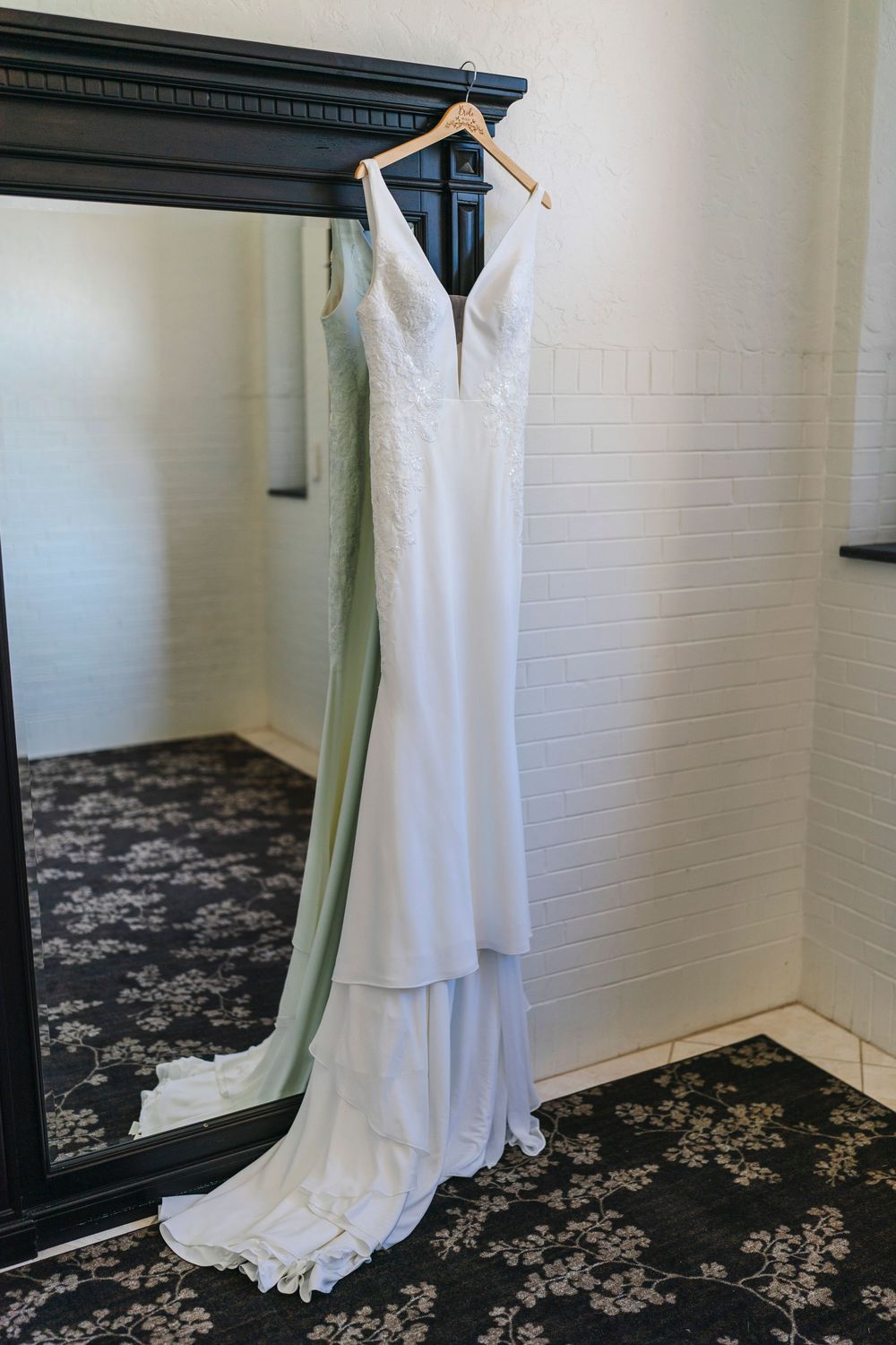 An elegant white wedding dress with a plunging v-neckline and flowing train hangs on display against a mirror.