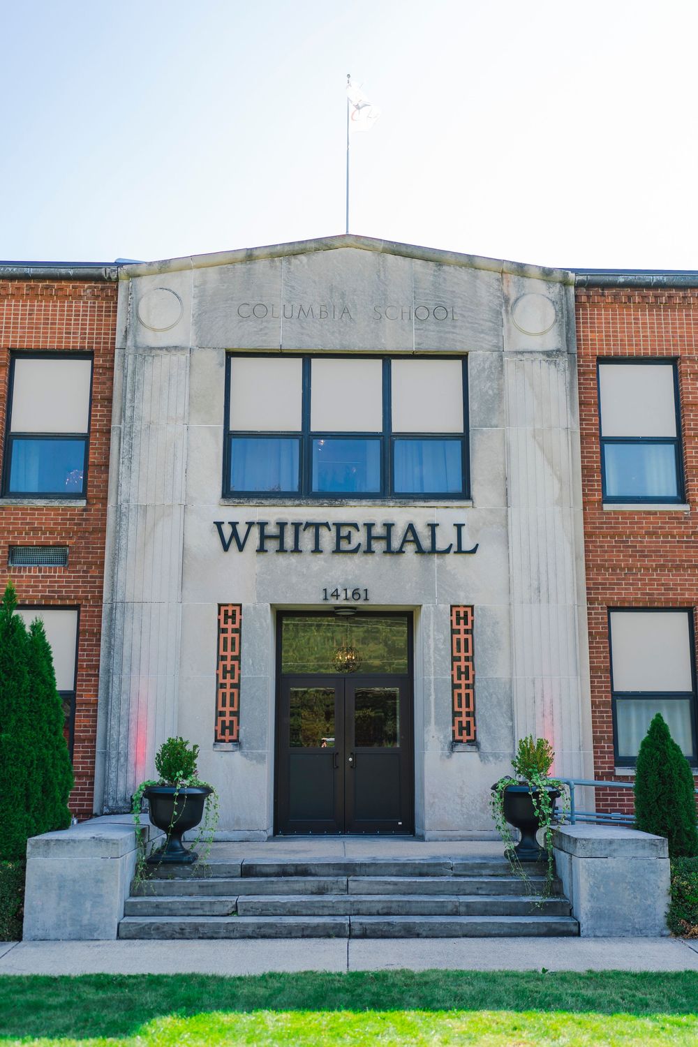 The entrance to Whitehall school featuring stone steps, decorative columns and potted plants at the doorway.