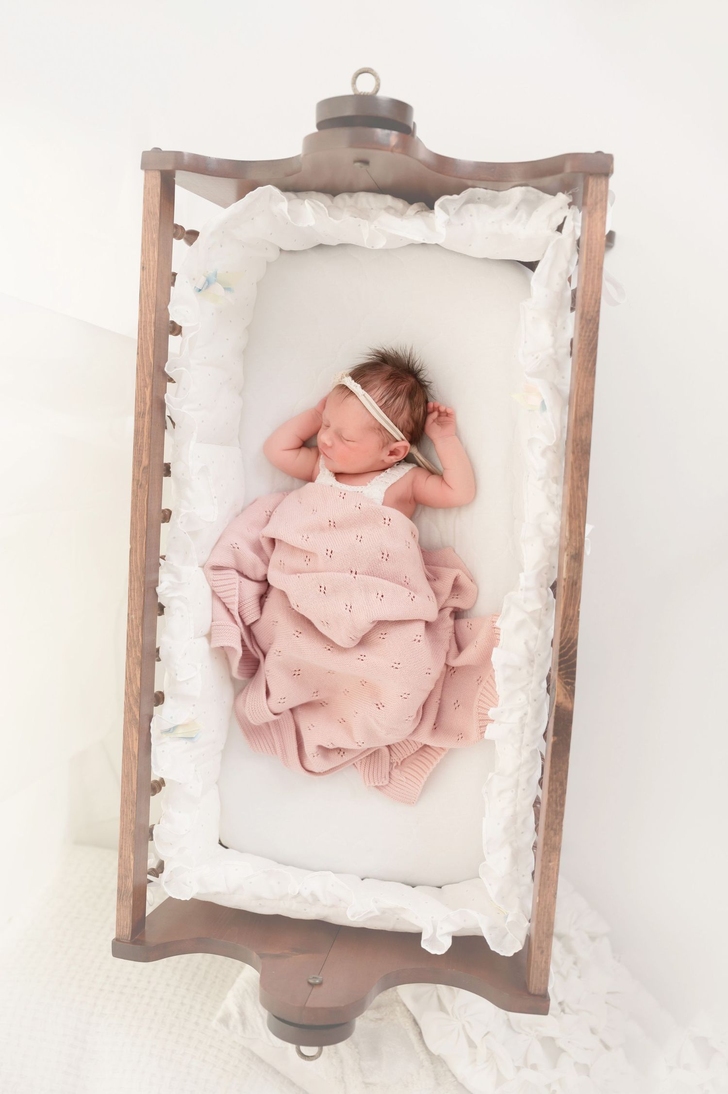 Four sequential photos of a newborn baby in pink clothing lying on white bedding in a wooden frame.