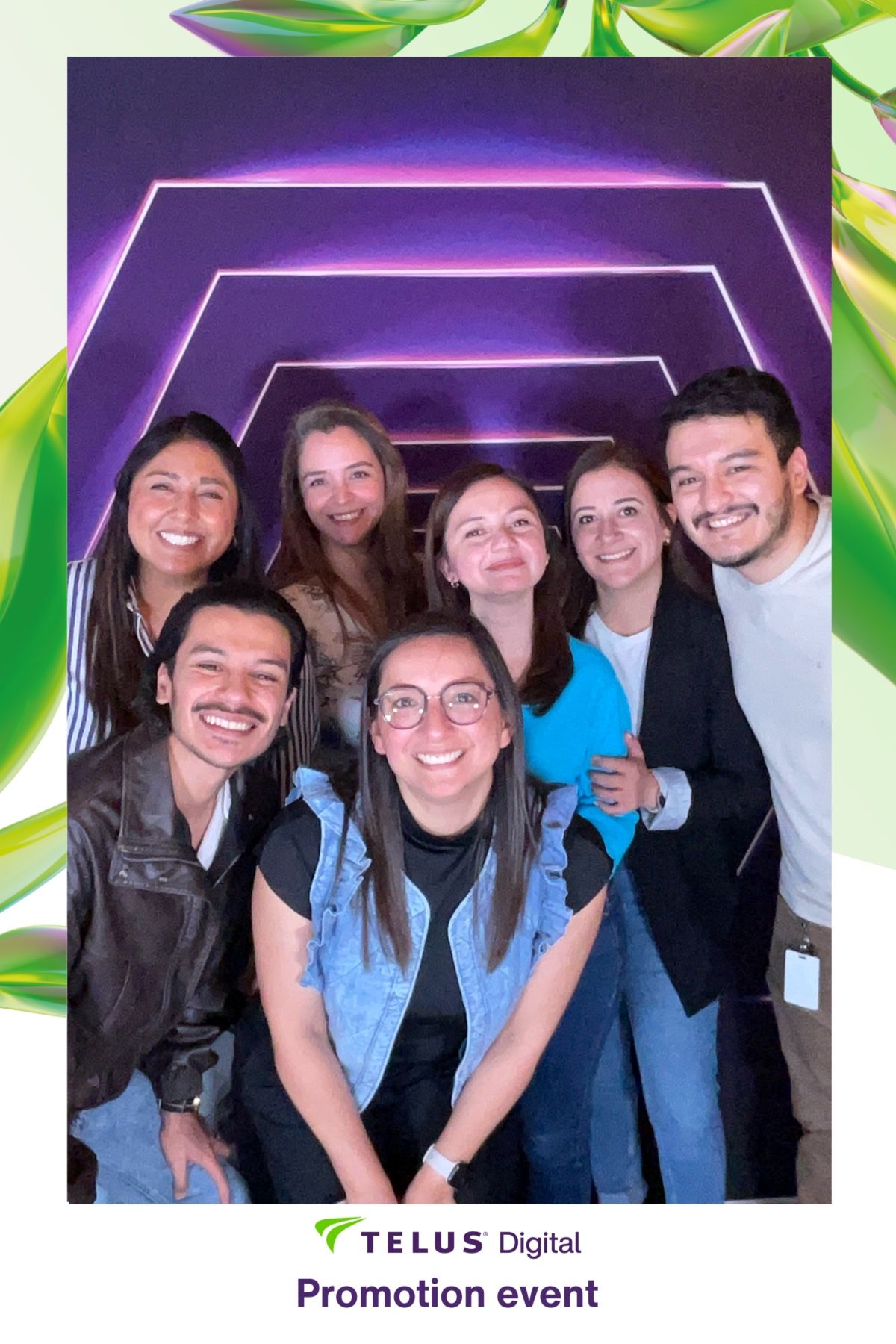 A group of colleagues smiling together at a TELUS Digital promotion event with purple lighting in the background.