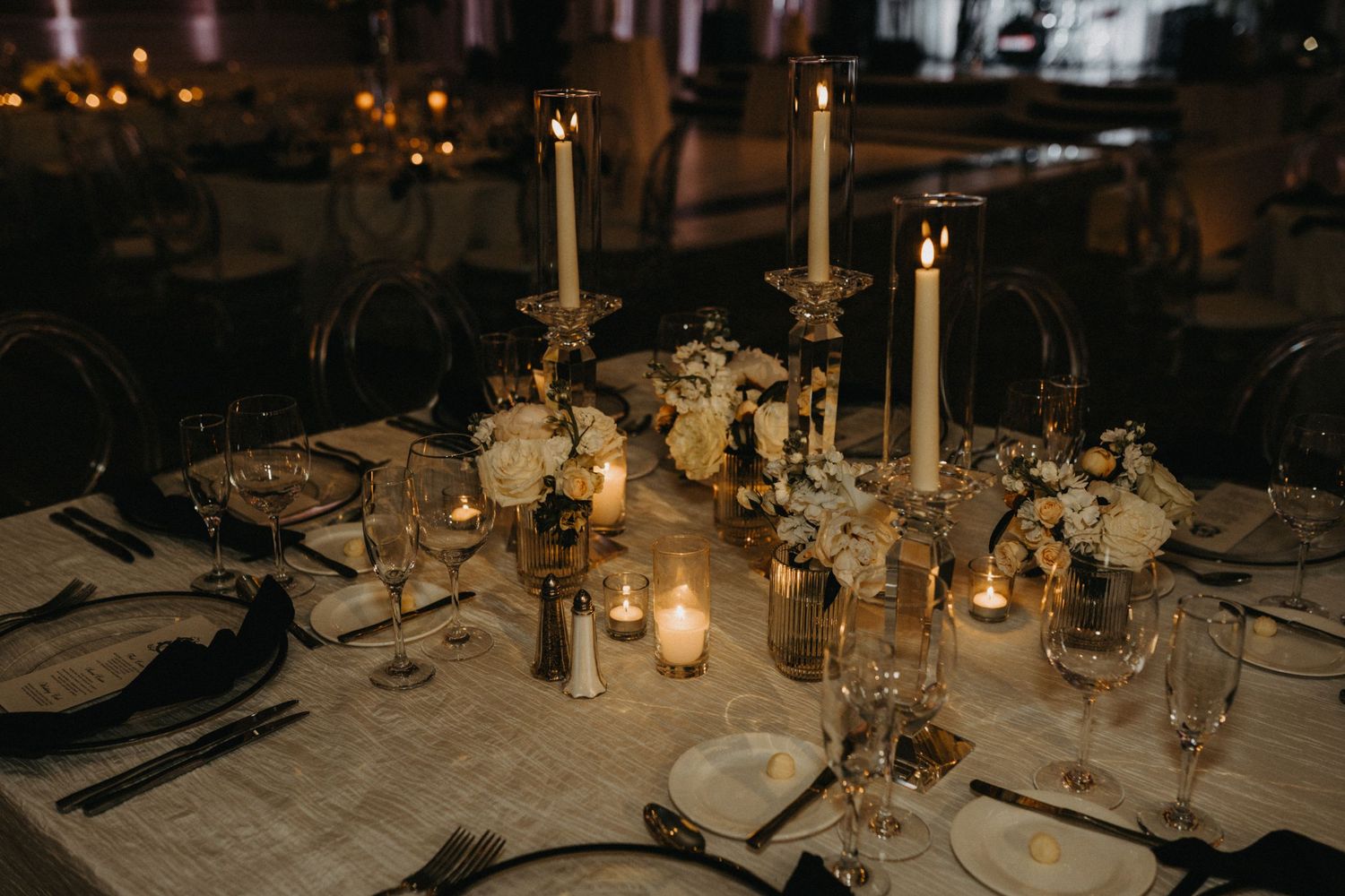 Elegant wedding reception table with tall taper candles, white floral centerpieces, and glowing votives on a white linen.