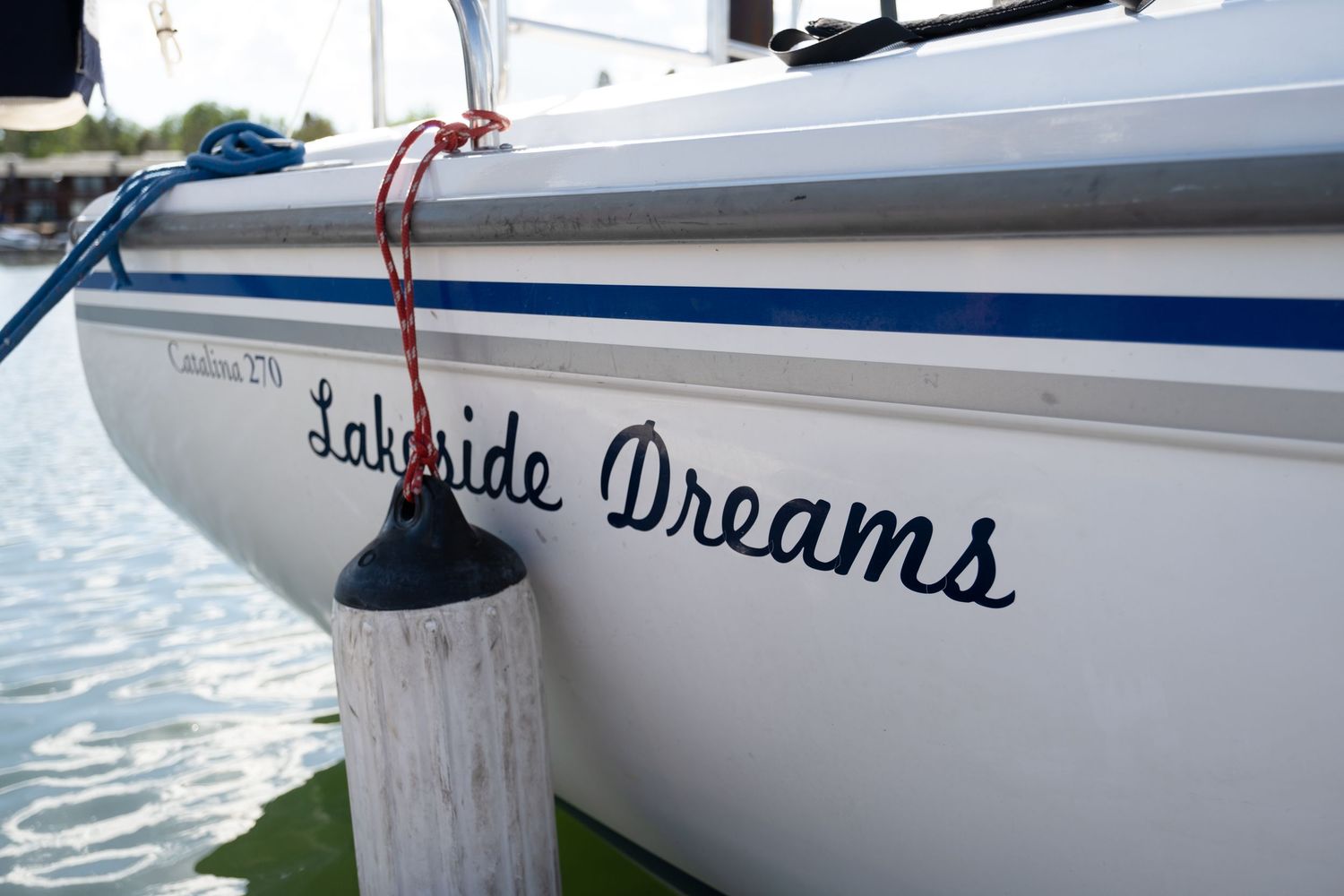 Close-up of a white sailboat named Lakeside Dreams docked at a marina, with blue trim and a red rope.