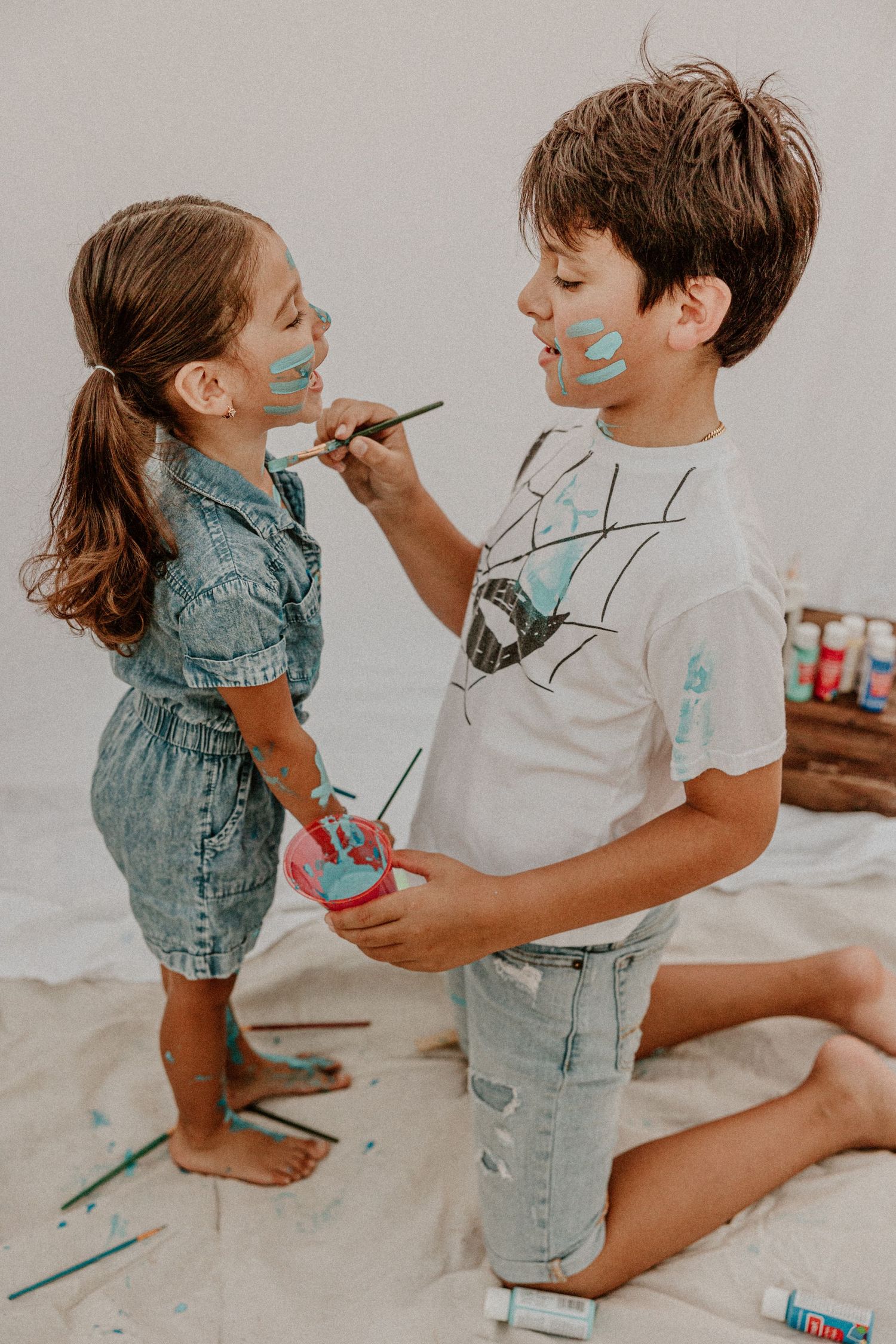 Two figures playfully paint each other's faces with bright blue paint while wearing casual clothes.