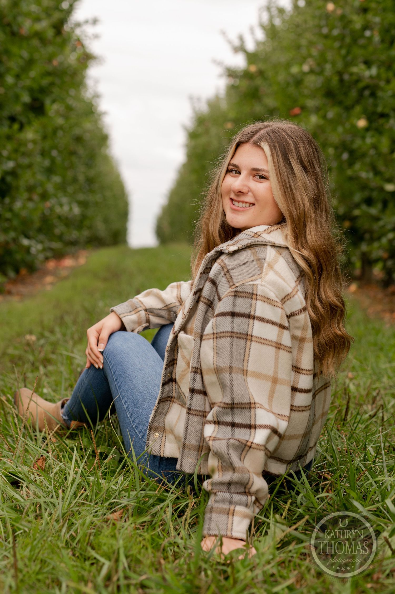 Candid autumn portrait of someone relaxing on grass in an apple orchard wearing plaid jacket.