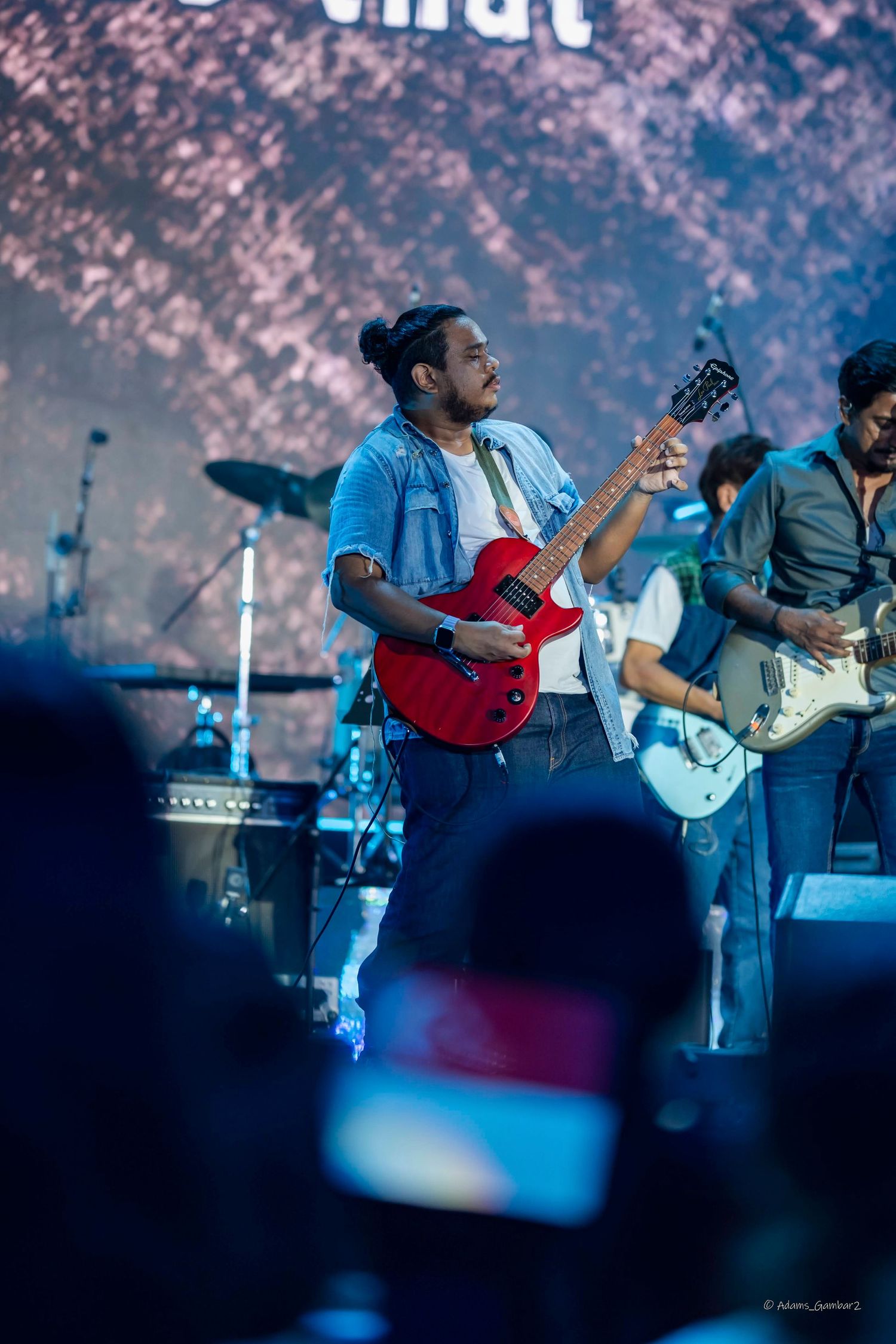 Guitarist in blue shirt plays red electric guitar during live performance.