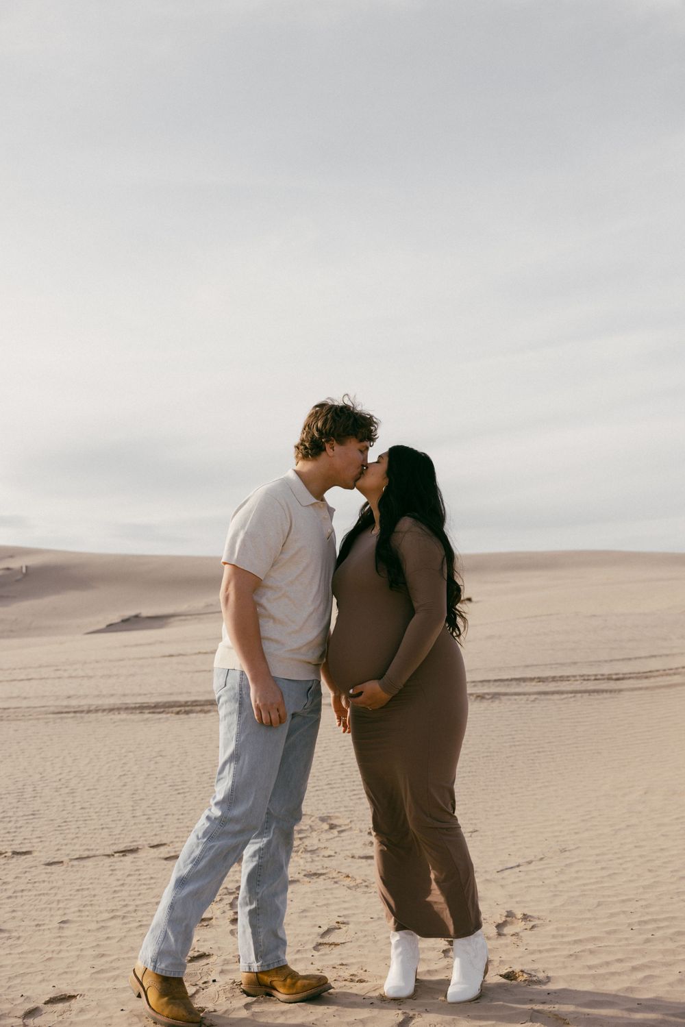Expectant couple sharing an intimate moment on sand dunes at sunset.