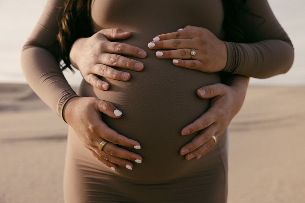 Close-up of hands tenderly cradling pregnant belly in desert setting.