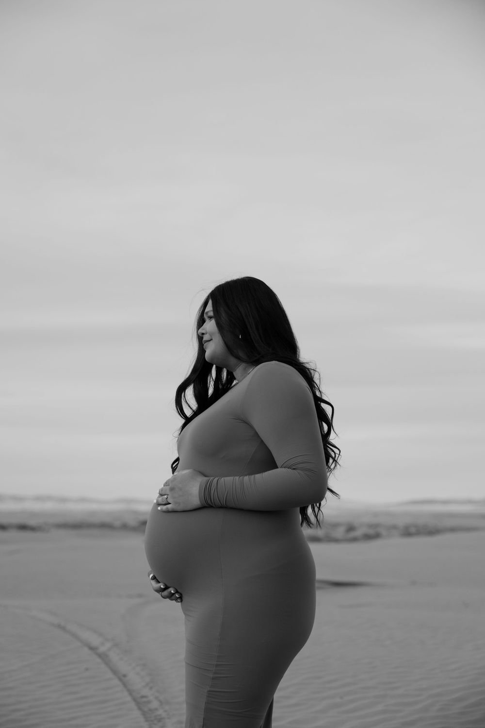 Silhouette of pregnant woman in form-fitting dress against desert landscape.