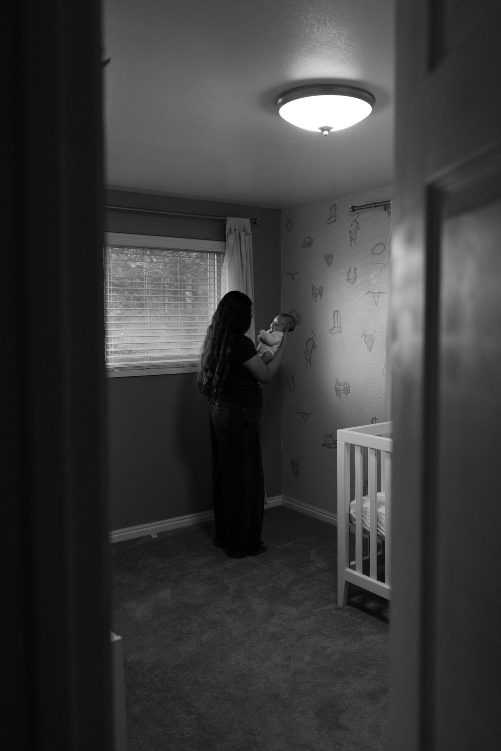 A person reads in a dimly lit nursery room with wallpaper and a crib visible.