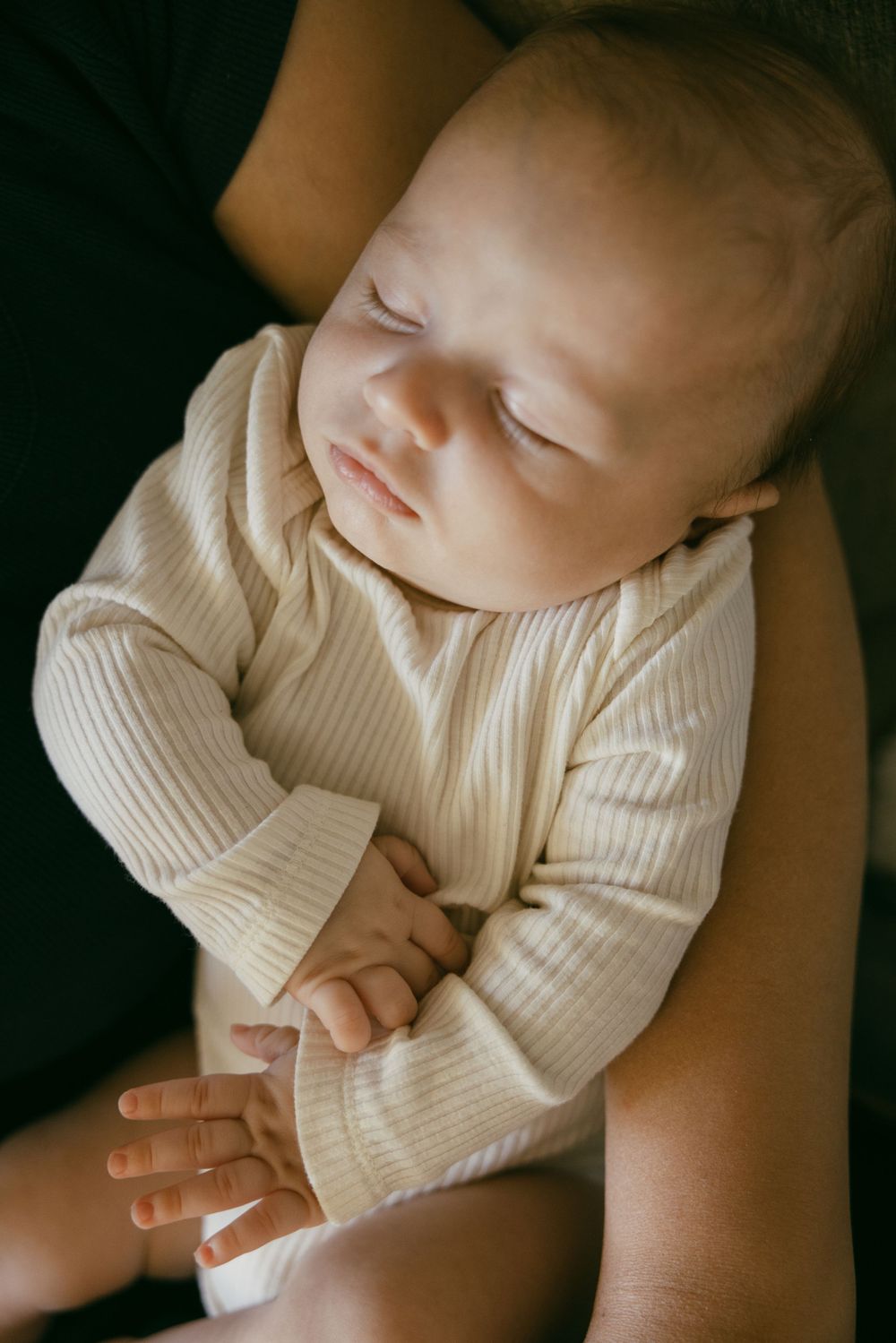 A peaceful sleeping baby in white clothing rests on dark fabric.