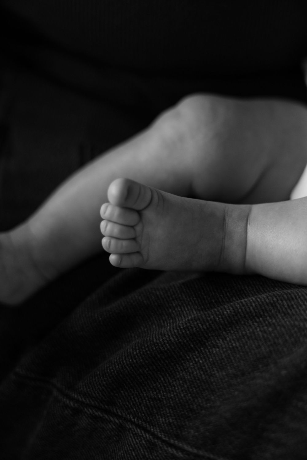 Close-up black and white photo of a tiny baby foot resting on dark fabric.