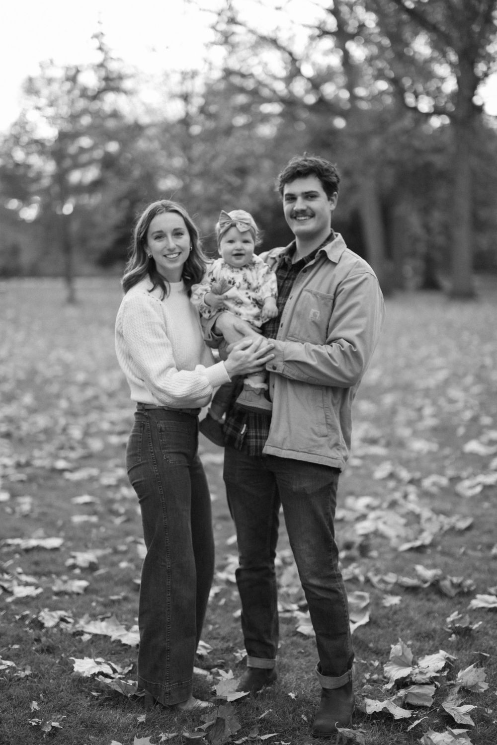 A family shares a tender moment together on fallen autumn leaves in a forest setting.