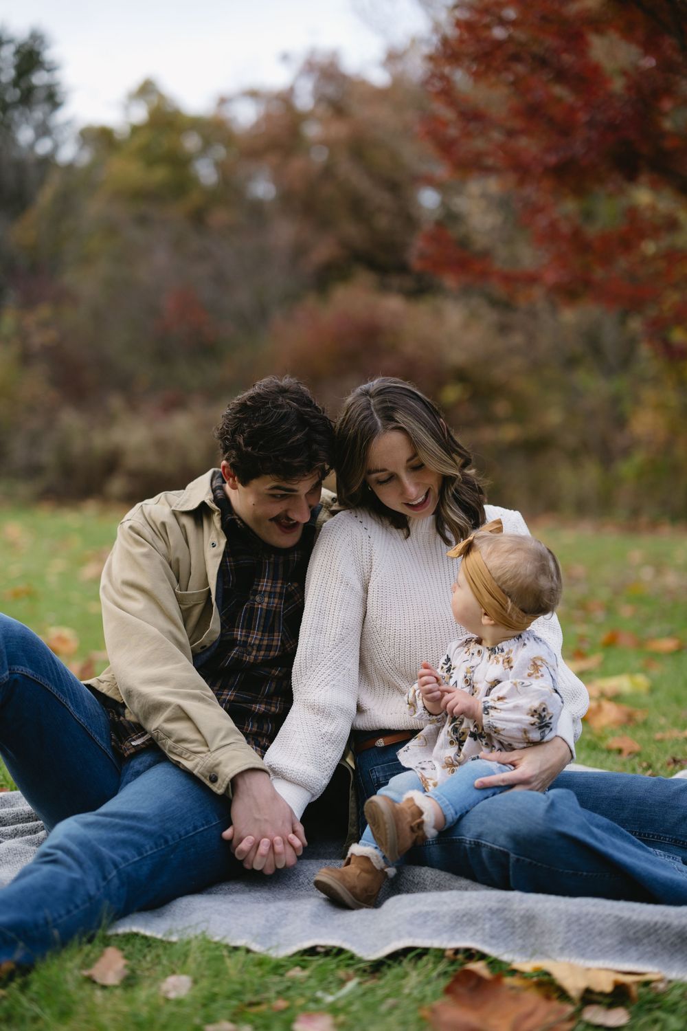 A family sits together on a blanket surrounded by colorful fall foliage.