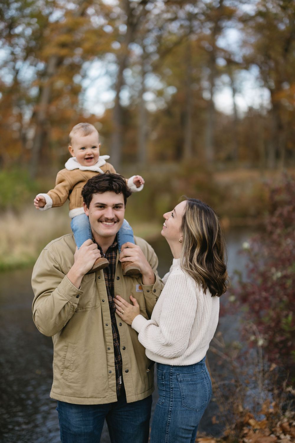 A family shares a joyful moment outdoors with their baby riding on shoulders.