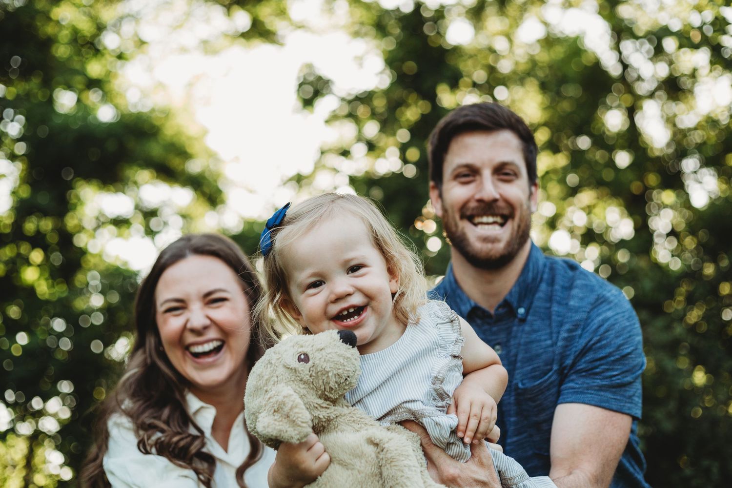 Happy family laughing together outdoors while holding stuffed animal toy.