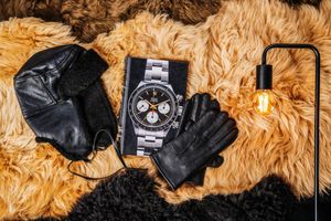 Luxury watch, leather gloves, and black face mask displayed on a fluffy beige and black fur background with industrial lamp.