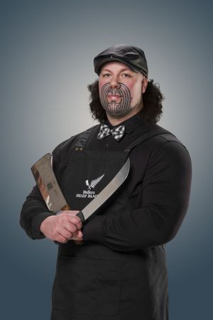 A portrait of someone wearing dark clothes with facial tattoos while holding a large knife.