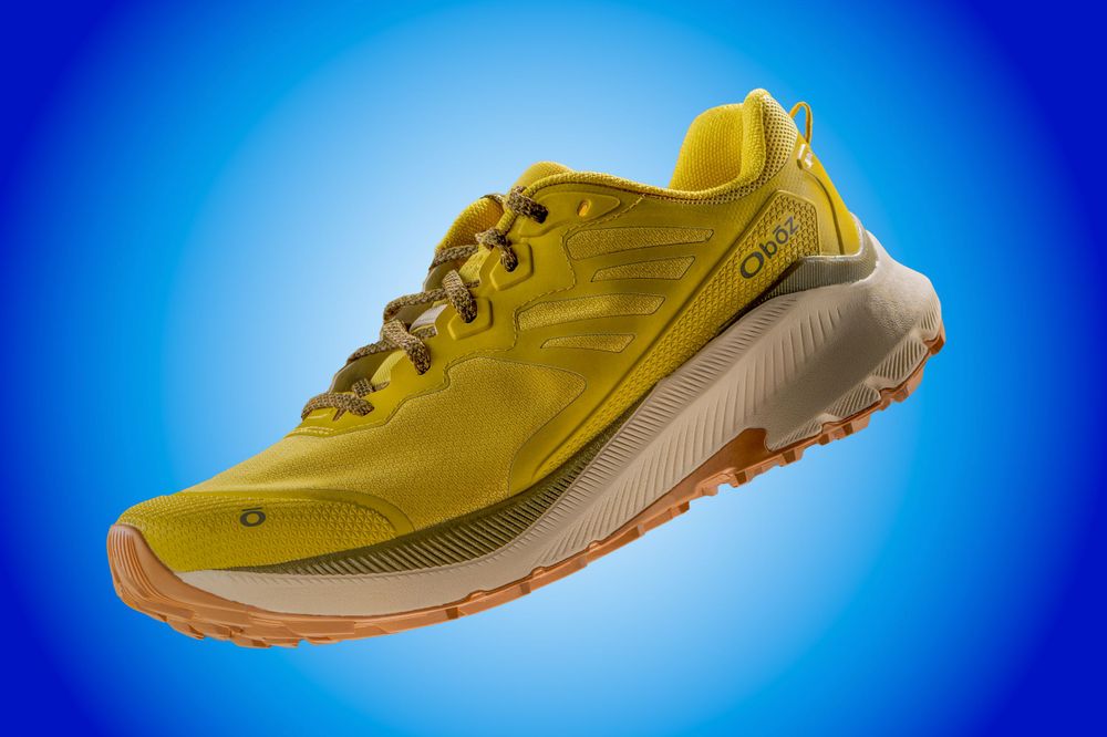 Yellow athletic running shoe photographed on blue gradient background.