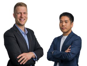 Two professional men in blazers posing with arms crossed against a white background.