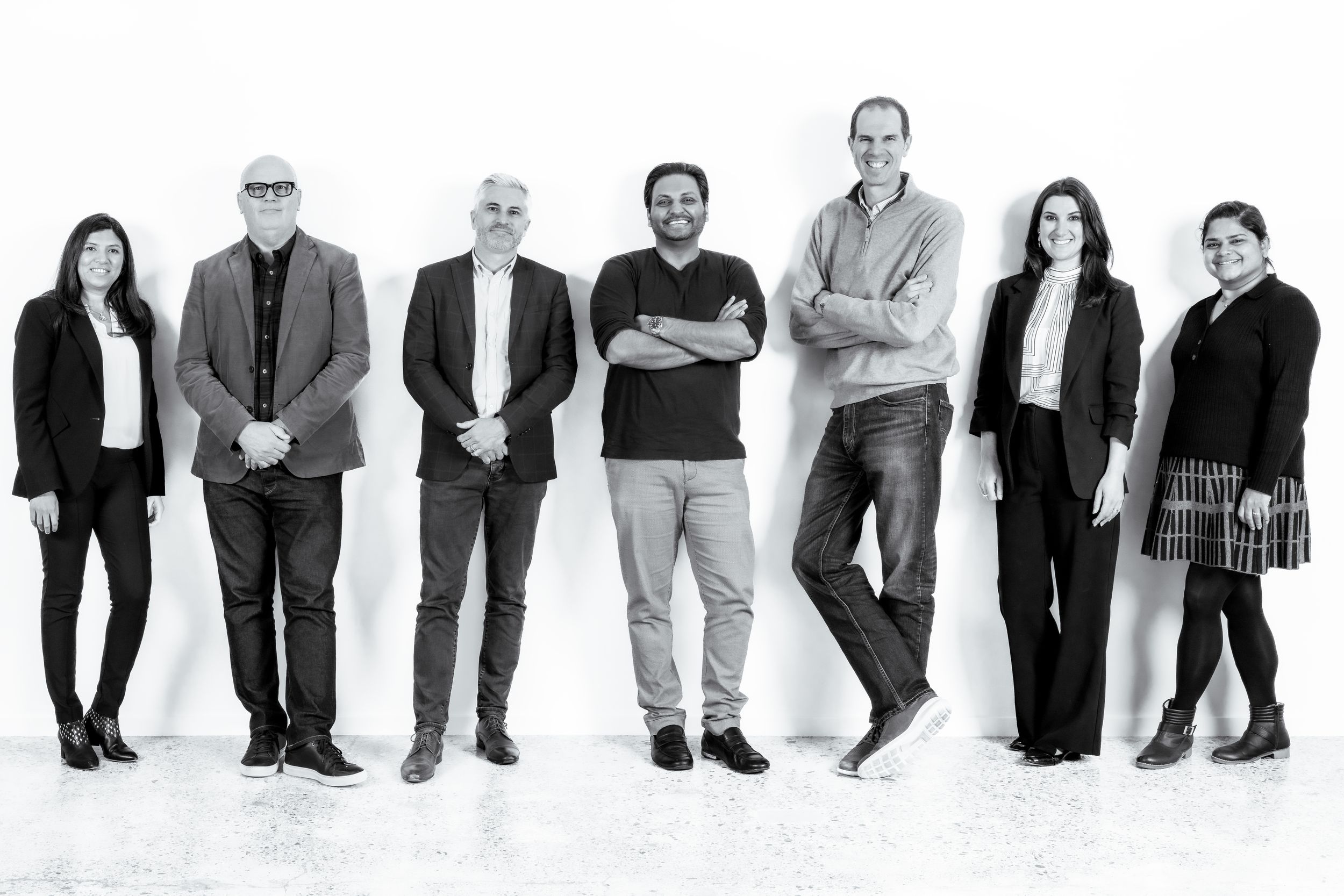 Black and white photo of seven diverse business professionals standing together in a modern studio setting.