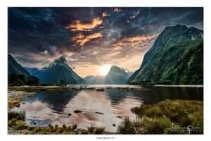 Dramatic sunset over Milford Sound in New Zealand with mountains reflecting in calm waters.