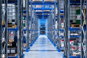 Long corridor in modern automated warehouse with blue metal storage racks and bright LED lighting on clean floor.