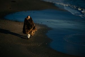 A person walks along a serene beach shoreline at sunset with their reflection visible in the wet sand.