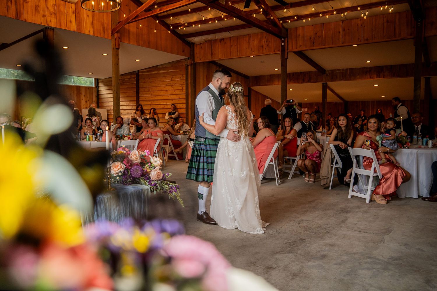 Couple shares first dance in rustic barn venue surrounded by seated guests.