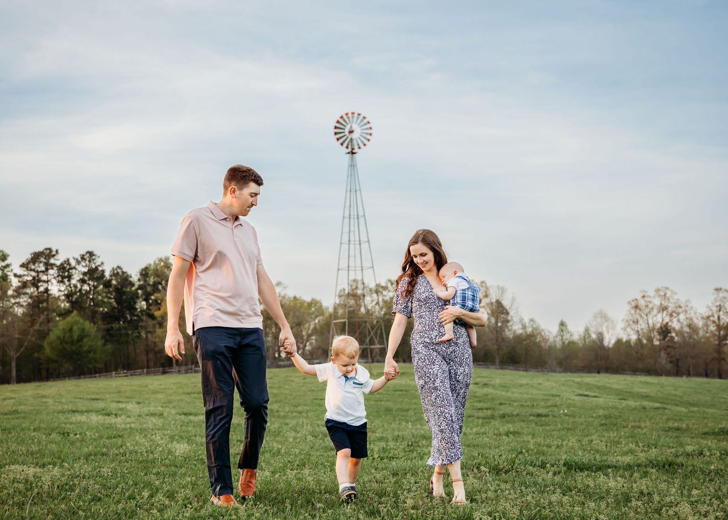 Family walks together across a green field with a windmill visible in the distance.