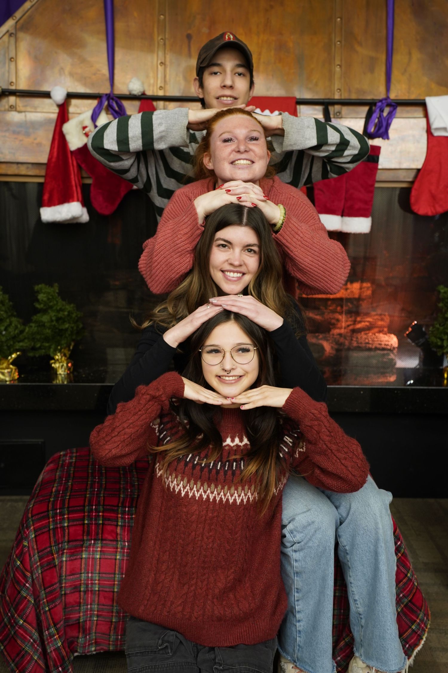Four people stacked on top of each other pose for a holiday photo by a fireplace with Christmas stockings.