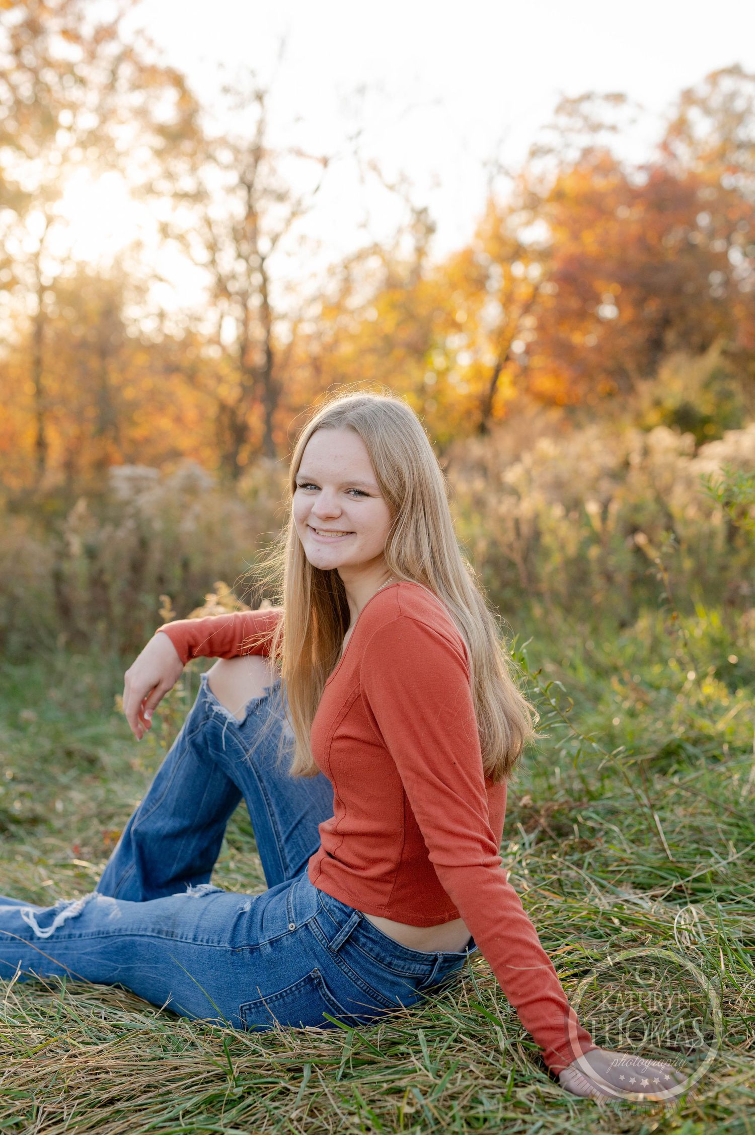 Casual autumn portrait sitting in grass wearing orange sweater and distressed jeans.