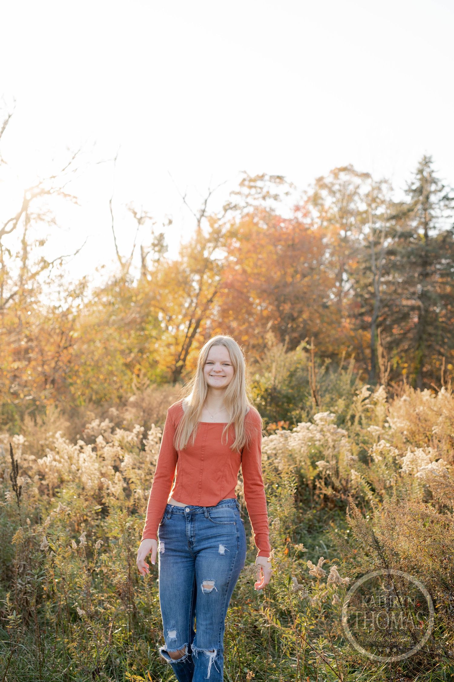 Outdoor portrait with orange sweater against autumn trees and golden grass.