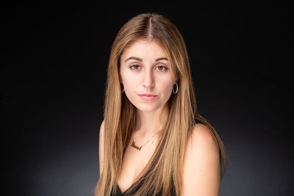 Dramatic studio portrait with dark background showcasing long blonde hair and delicate jewelry.