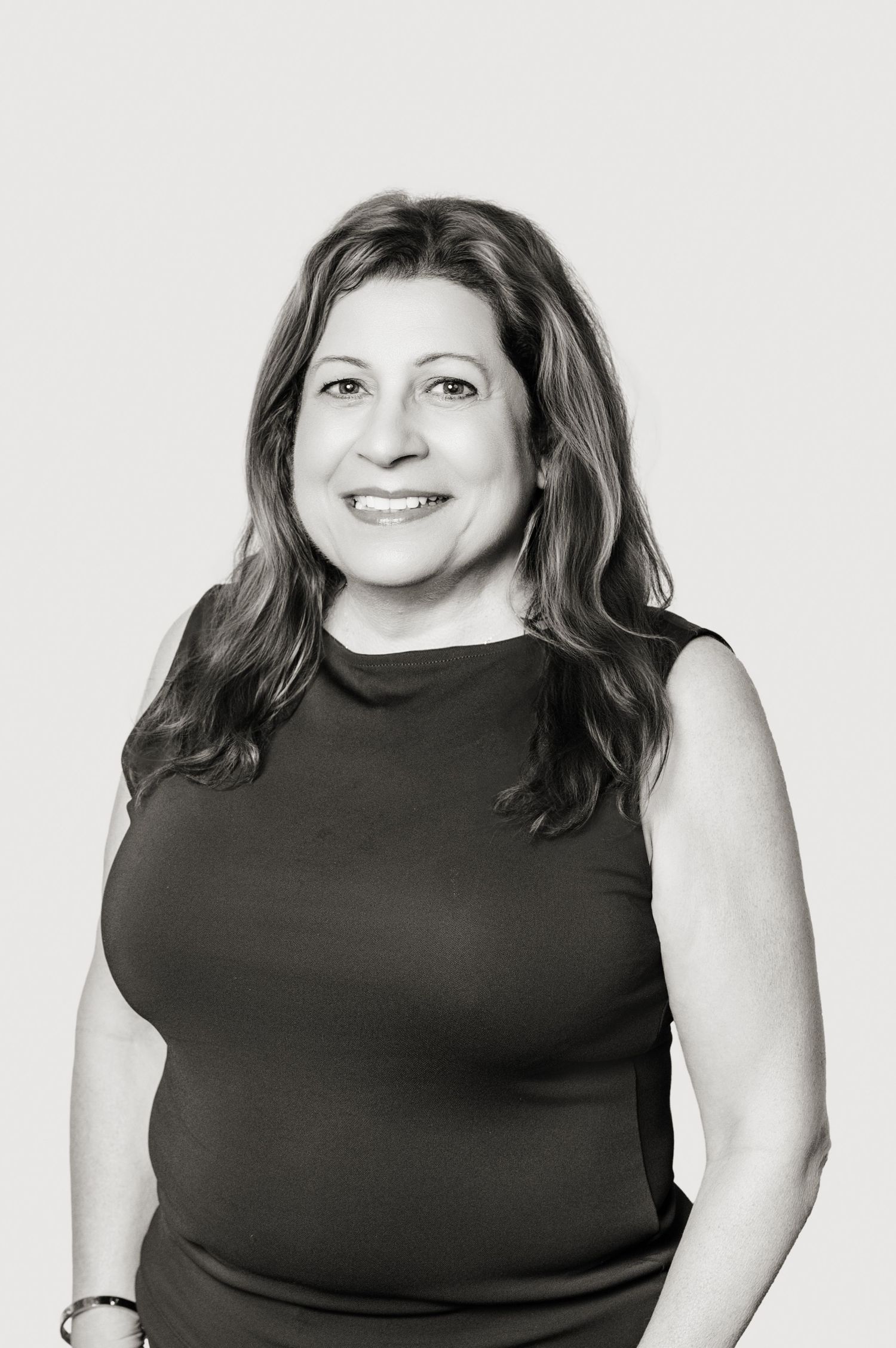 A black and white professional portrait of a smiling woman with long wavy hair wearing a sleeveless dark top.