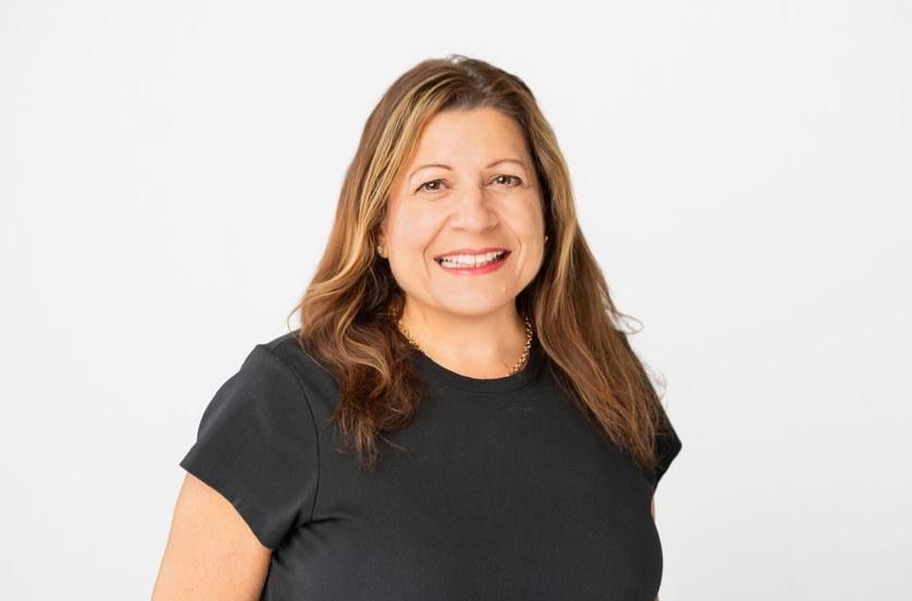 Smiling woman with brown hair wearing a black t-shirt poses for a professional headshot against a white background.