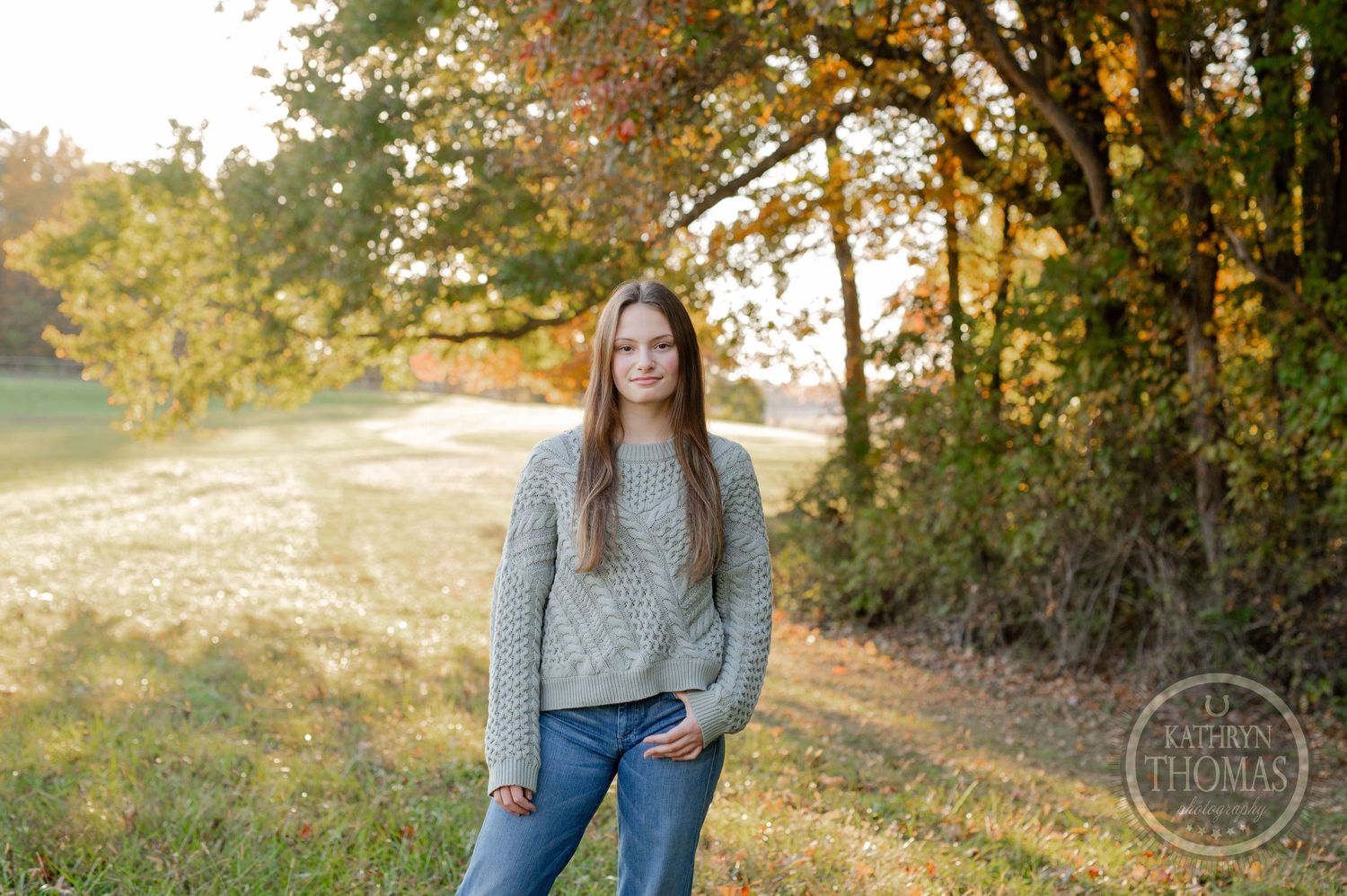 A casual portrait of someone in a gray sweater standing in a sunlit autumn field.