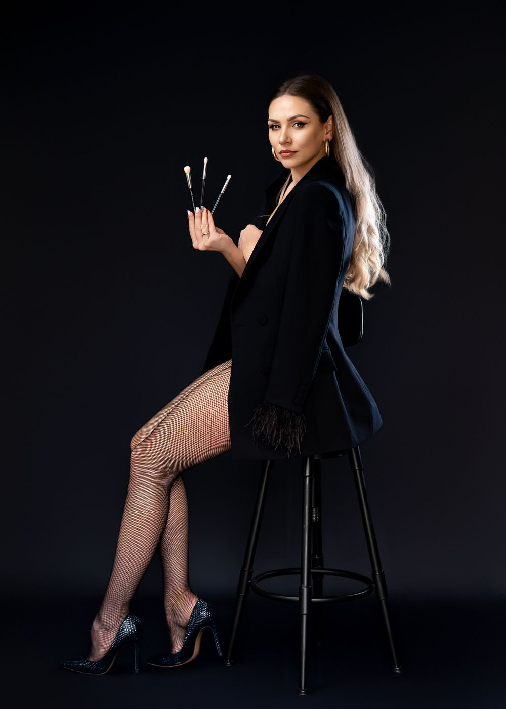 Glamour portrait of woman in black blazer and fishnet stockings on bar stool.